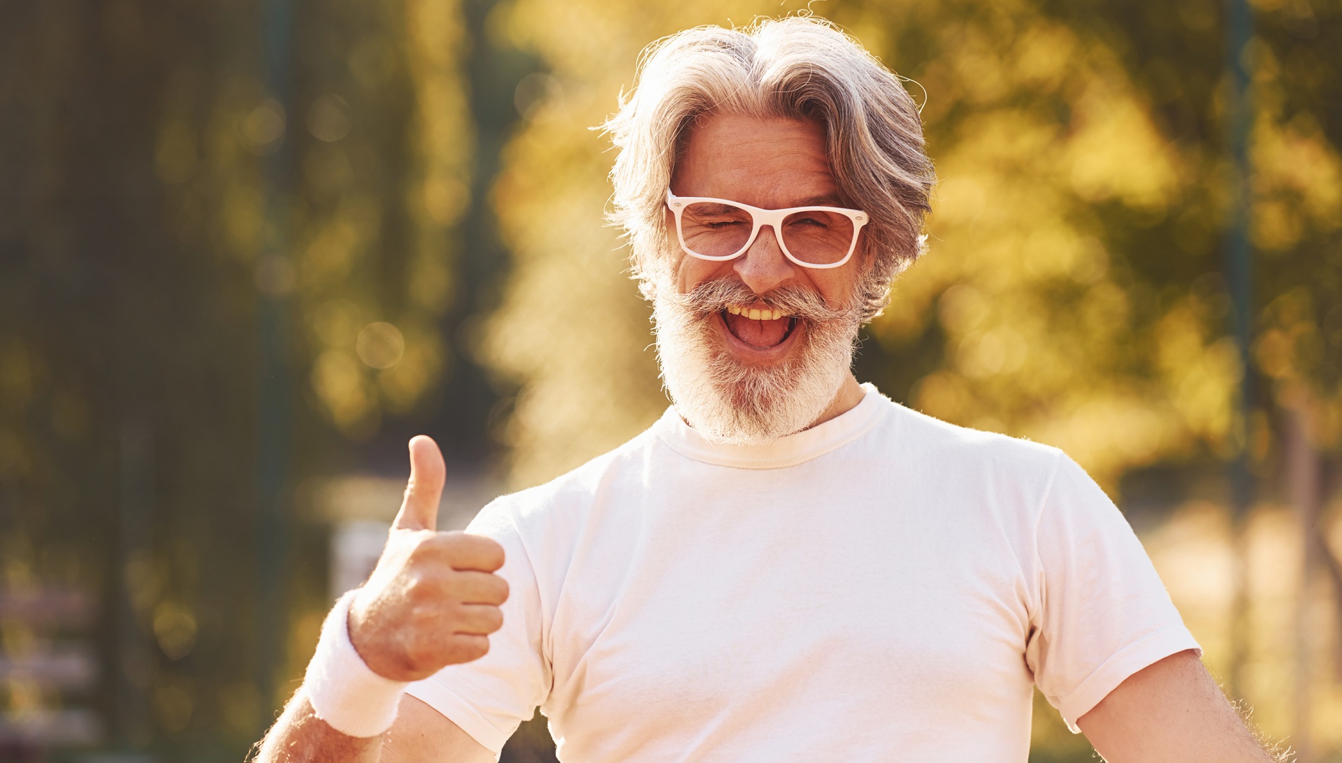 Senior stylish man in eyewear, white shirt and black sportive shorts on tennis court